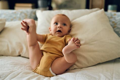 Dojenček leži na hrbtu in se igra z nogami