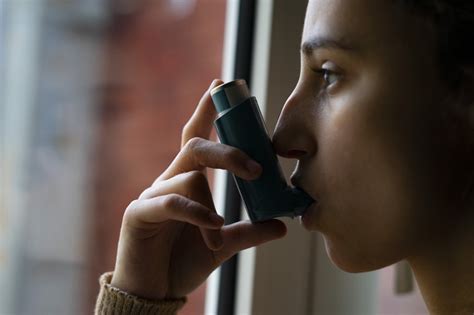 Ženska, ki drži v roki inhalator za astmo, medtem ko gleda v nosečniški trebuh.