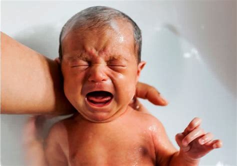 Novorojenček v naročju matere, ki ga nežno gleda.