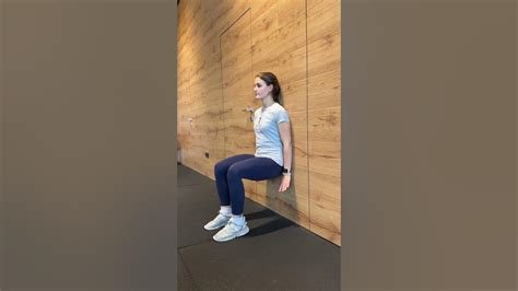 Nosečnica izvaja počep z žogo ob steni, vaja za stabilnost in sproščanje hrbta