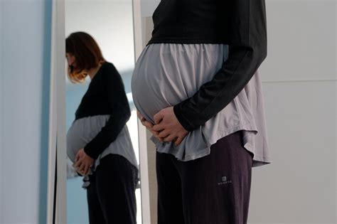 Nosečnica, ki se gleda v ogledalo z nasmehom, oblečena v stilsko nosečniško bluzo