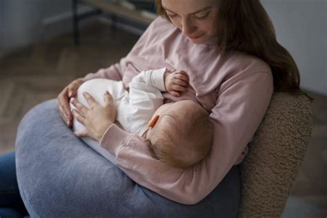 Mama doji dojenčka, ki leži na blazini za dojenje, ki ji podpira hrbet in roke.